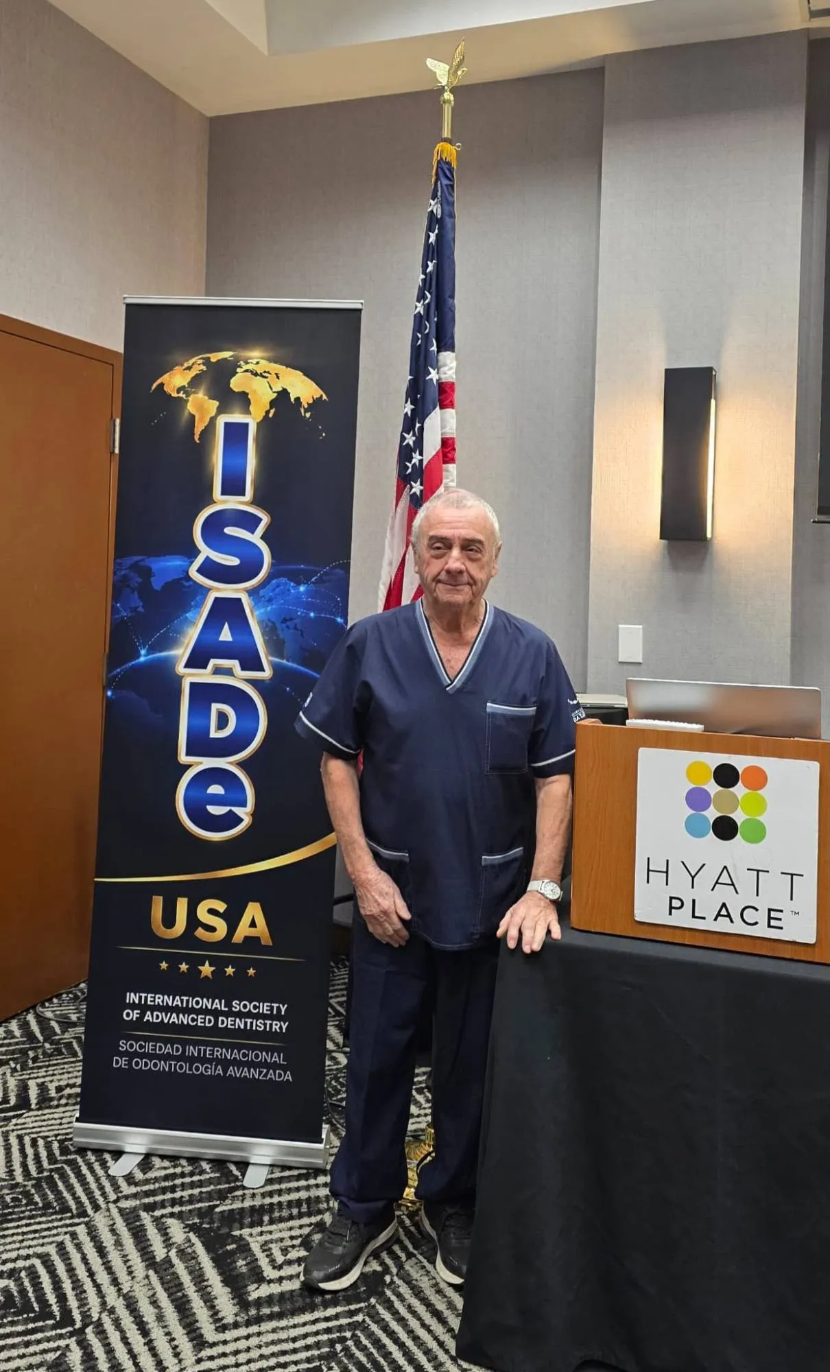 A speaker beside the ISADe USA banner and the United States flag.